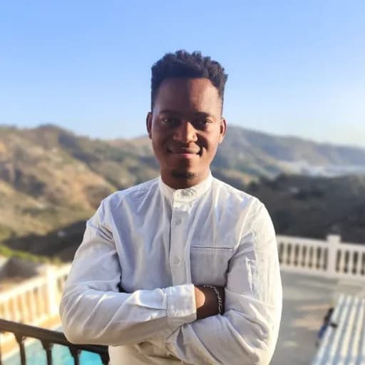 Jay, de brazos cruzados, sonriendo, en una terraza frente a las montañas